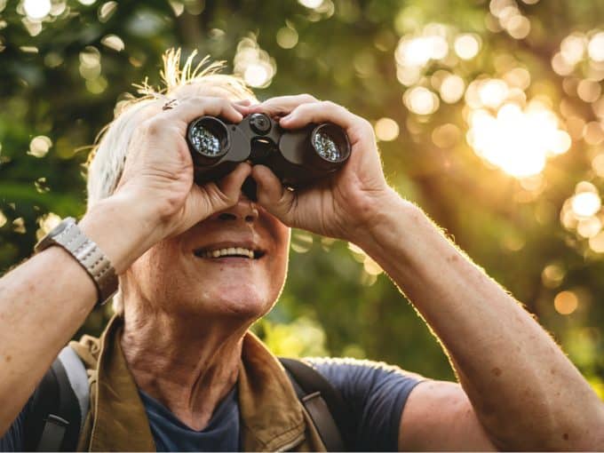 Eine ältere Frau beobachtet mit ihrem Fernglas etwas in der Natur.
