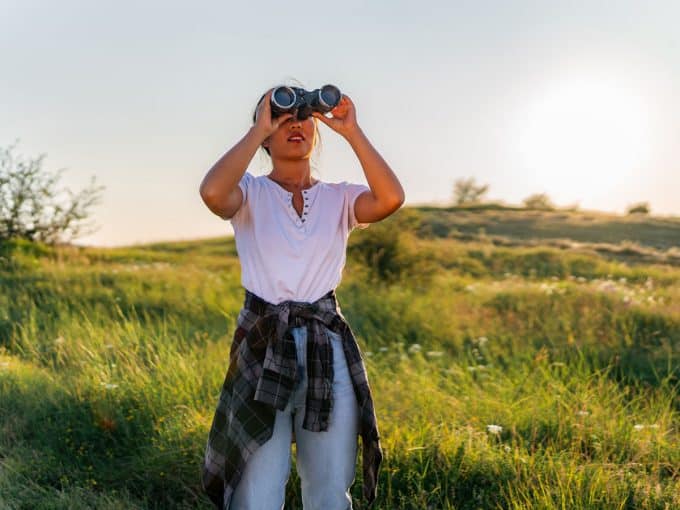 Eine Frau schaut durch ihr Fernglas in die Natur.
