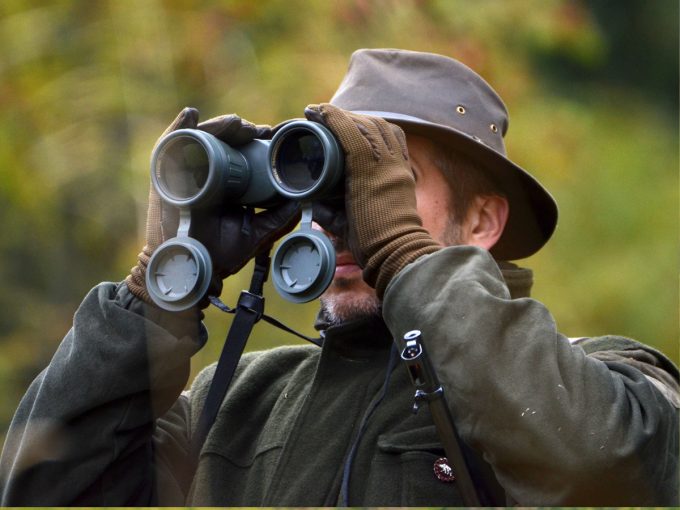 Ein Jäger schaut konzentriert durch sein Fernglas.