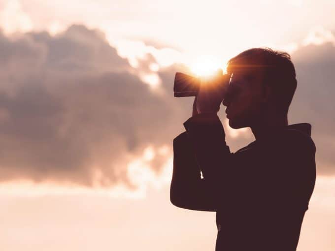 Ein Mann steht vor einem wolkenbedeckten Himmel und schaut durch sein Fernglas.