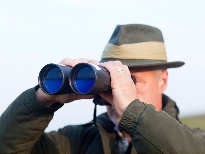 Ein Jäger schaut durch sein Fernglas während er auf der Jagd ist. 
