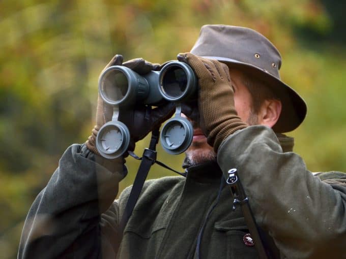 Ein Jäger schaut durch sein Fernglas und beobachtet etwas in der Ferne.