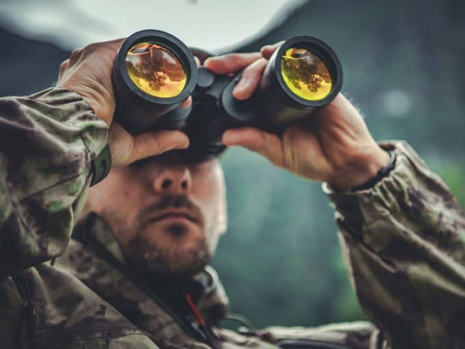 Ein Jäger beobachtet mit seinem Fernglas das Wild.
