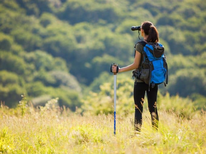 Eine Frau steht auf einer Wiese und beobachtet mit ihrem Fernglas die Natur.