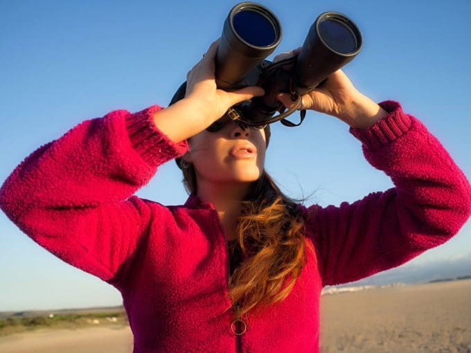 Eine Frau steht in der Natur und schaut durch ihr Fernglas.