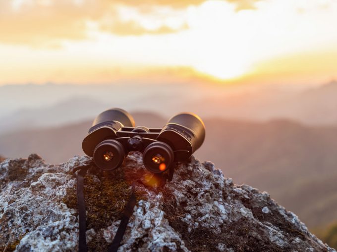 Ein Fernglas liegt auf dem Gipfel eines Berges und es kann der Sonnenuntergang beobachtet werden. 